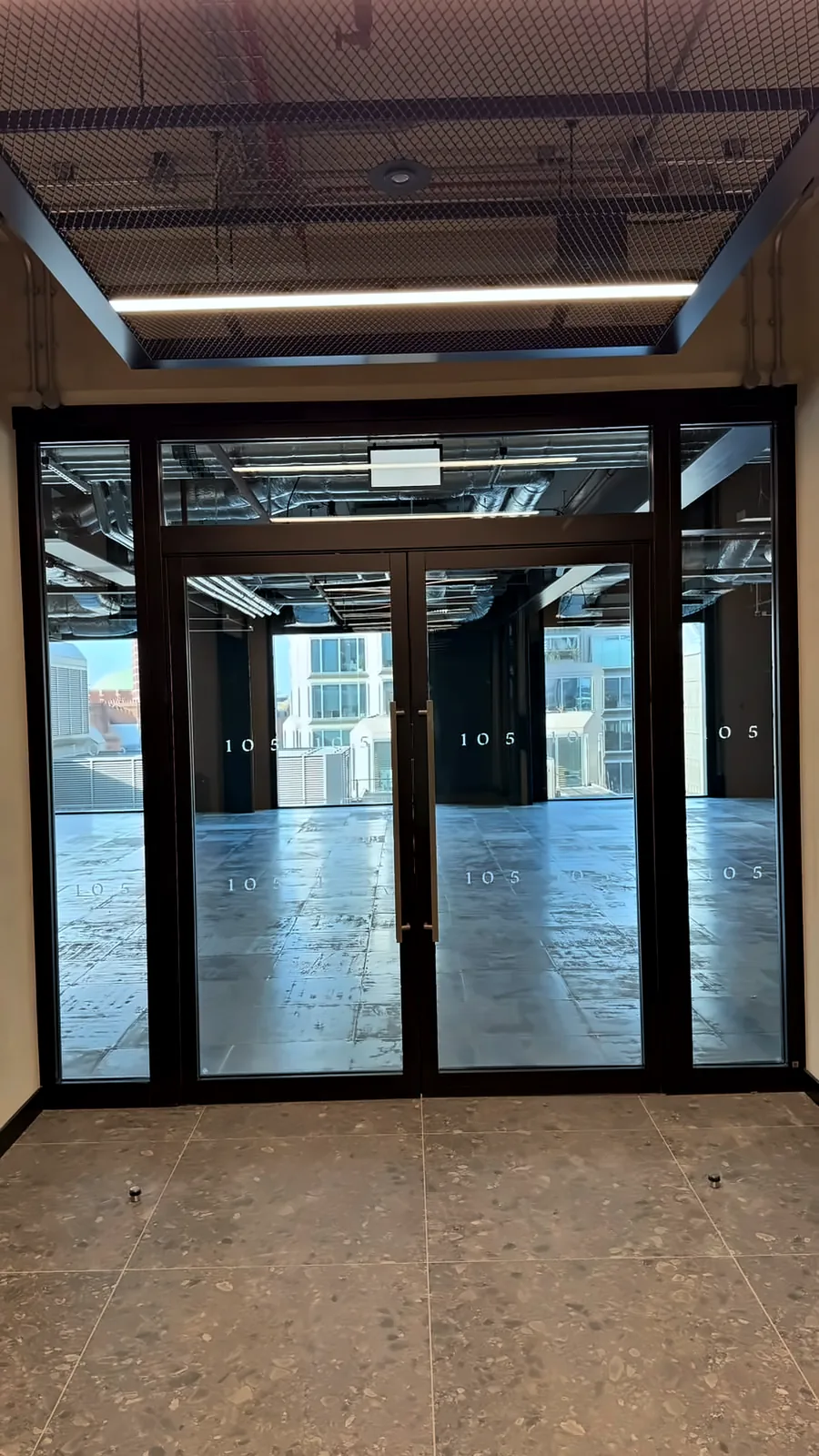 Black-framed glazed fire doors and screens at a lift core lobby, opening onto the office floor at 105 Victoria.