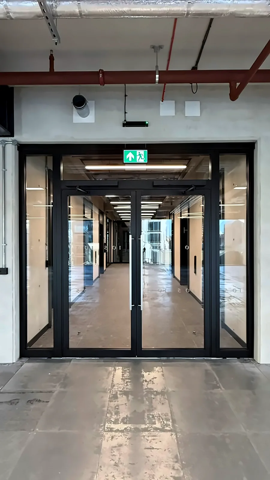 Lift lobby fire doors under the exit sign, with the corridor beyond.