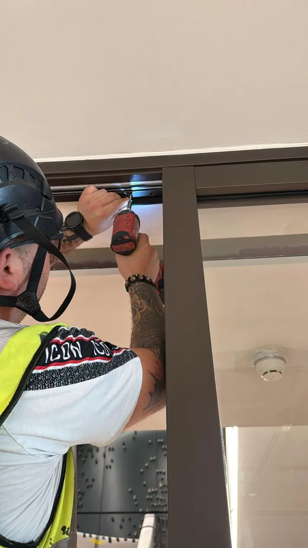 An OMFC installer fixing the head of a door frame with a cordless driver.