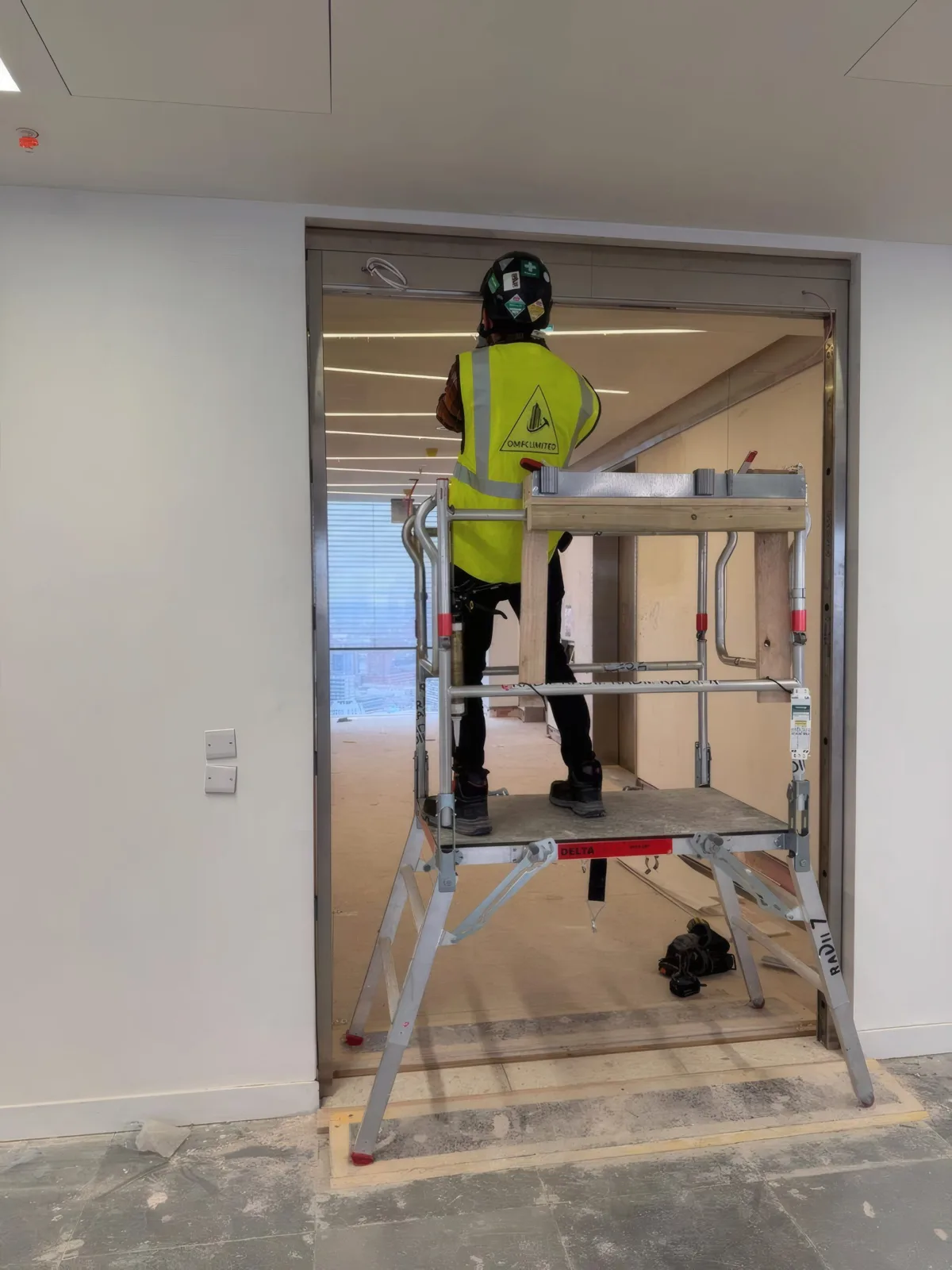 Fitting the head of a fire door frame from a podium step, ahead of glazing.