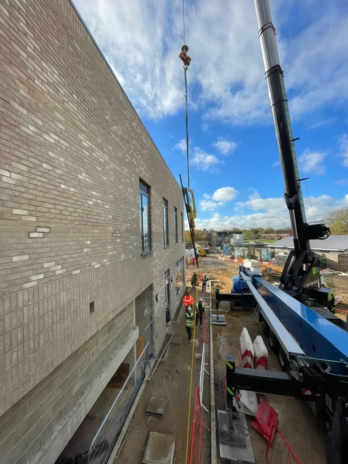 A glazing unit being craned up the facade, guided by the OMFC International team below.