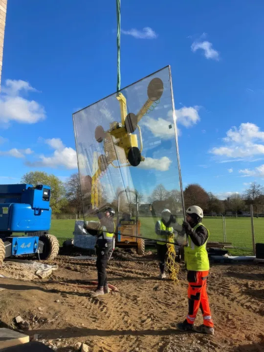 A glazing unit on a vacuum lifter against a blue sky in Cambridge.