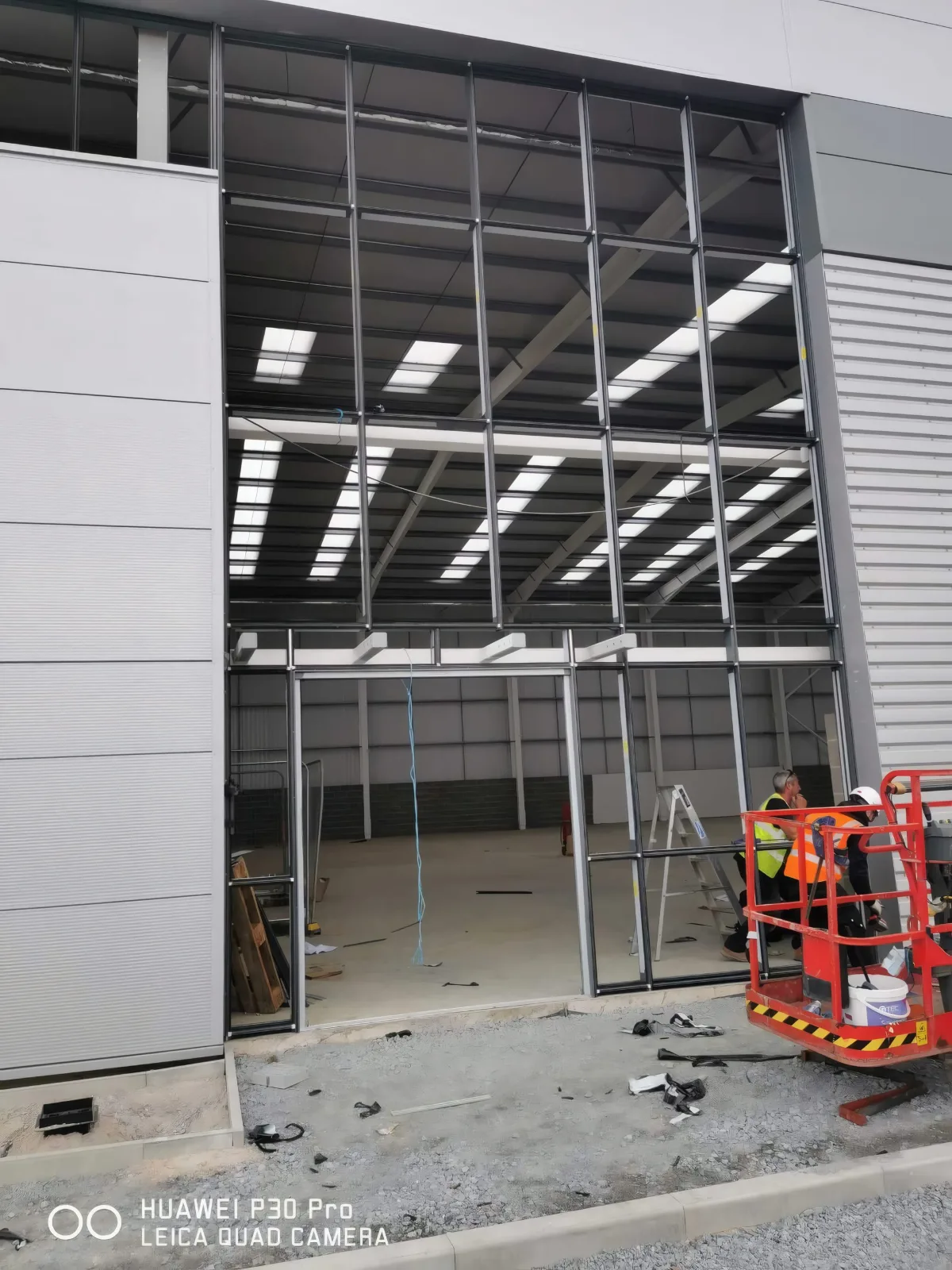 Installers on a mobile access platform at a full-height glazed frame.