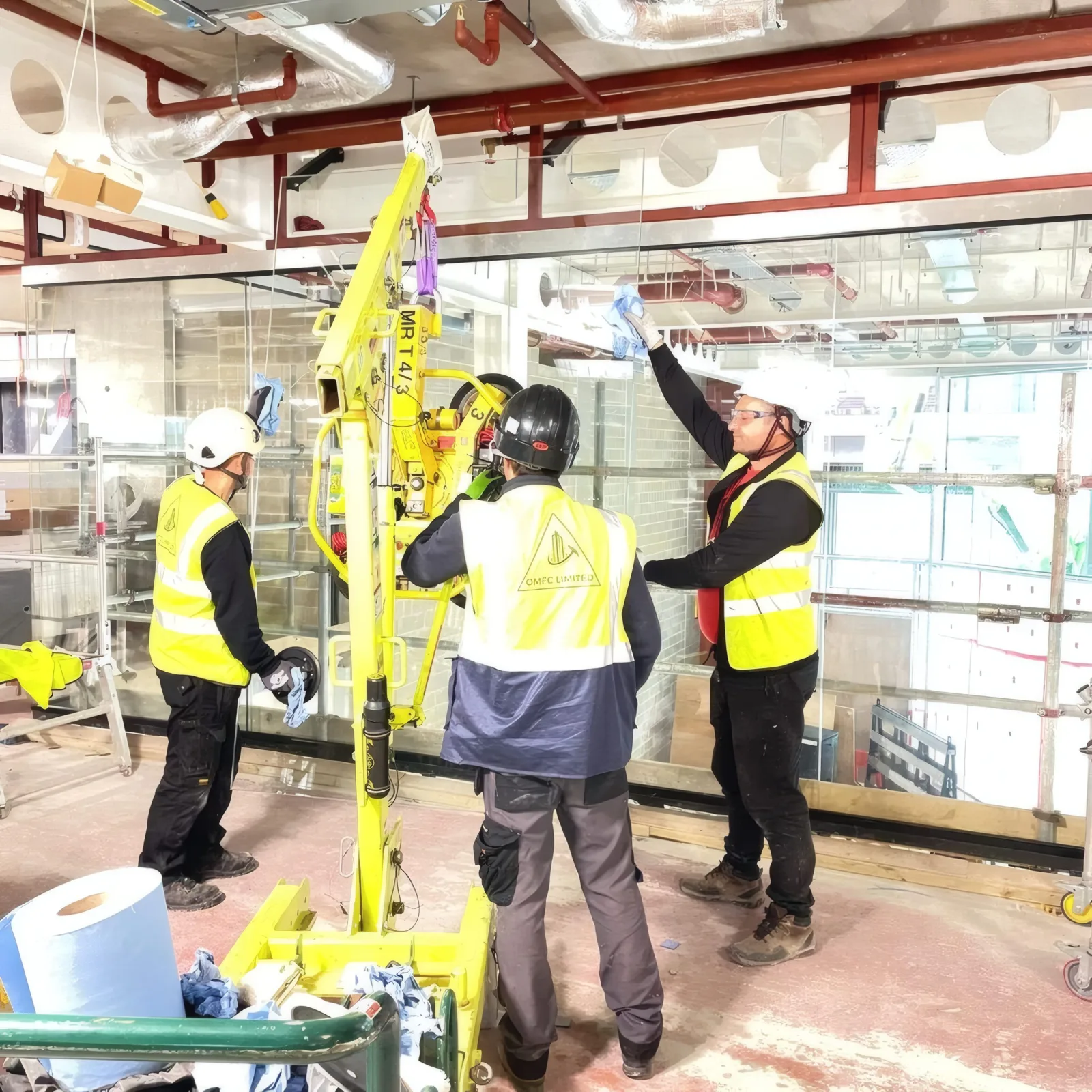 The OMFC International site team lifting a glazed screen panel into position using a vacuum lifting crane.