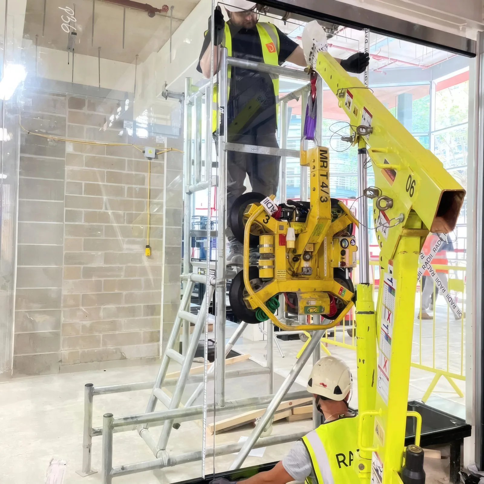 A glazed screen panel being lifted into position using a vacuum lifting crane, guided from a podium platform.