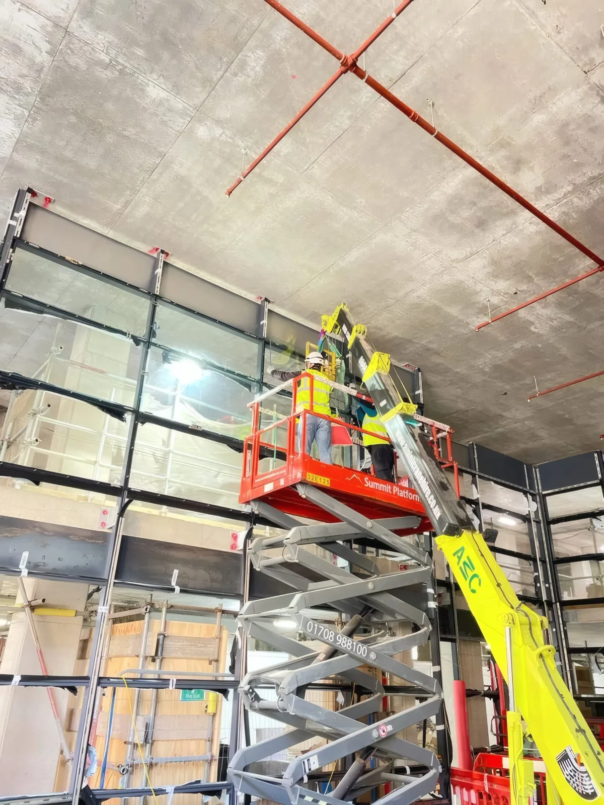 Positioning a steel member into the curtain wall grid using a spider crane and mobile access platform.