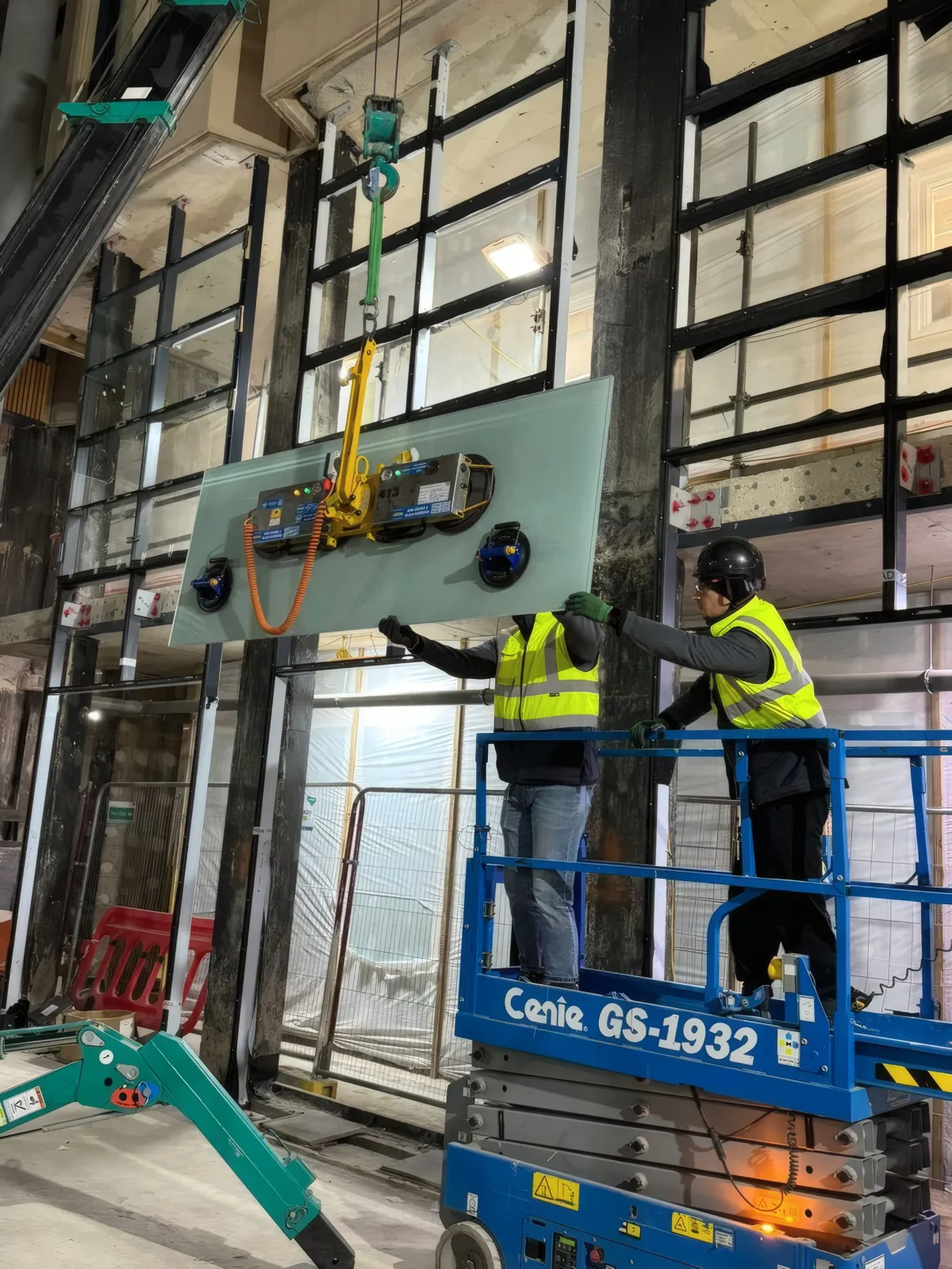 A glazing unit being lifted into the facade frame using a vacuum lifter, guided by two installers.