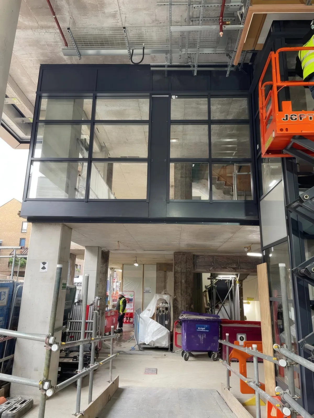 A black-framed glazed box at first-floor level, framed and glazed, with a MEWP alongside.