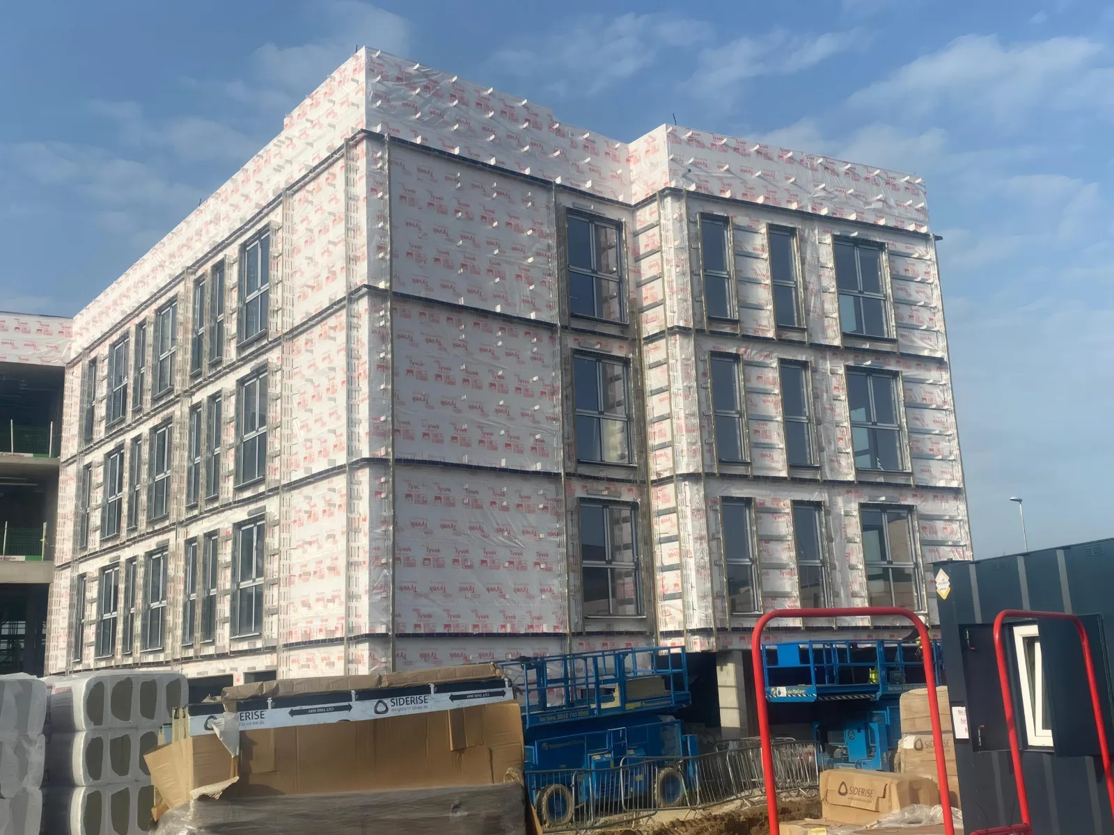 The structure wrapped in breather membrane, with windows fitted and insulation stacked on site.