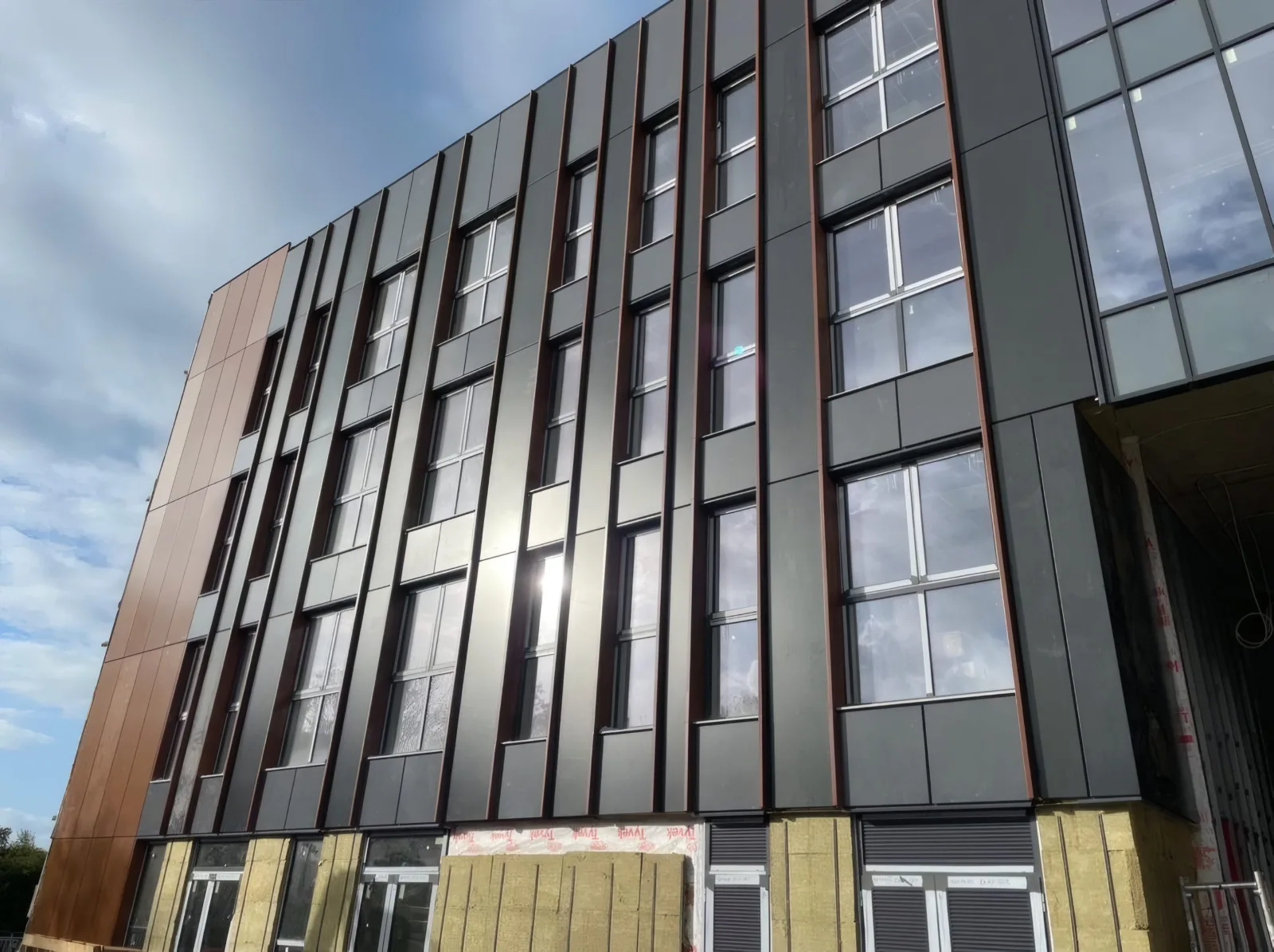 A completed elevation of dark and copper-coloured cladding panels, with insulation still exposed at ground level.