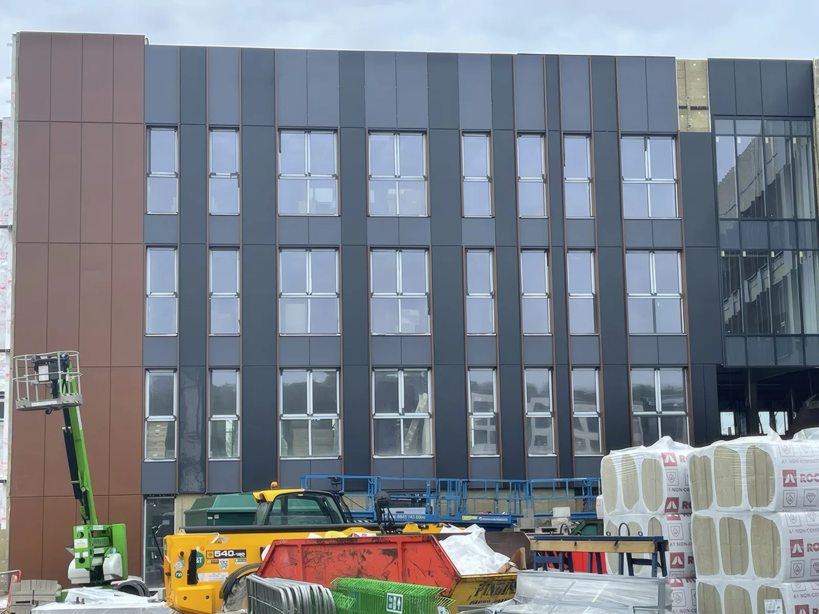 A clad elevation, with access equipment and deliveries in front.
