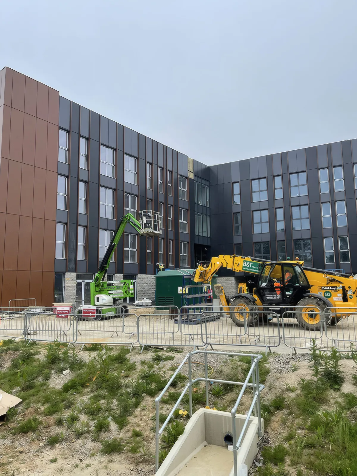 The main elevations, with a telehandler and boom lift on site.