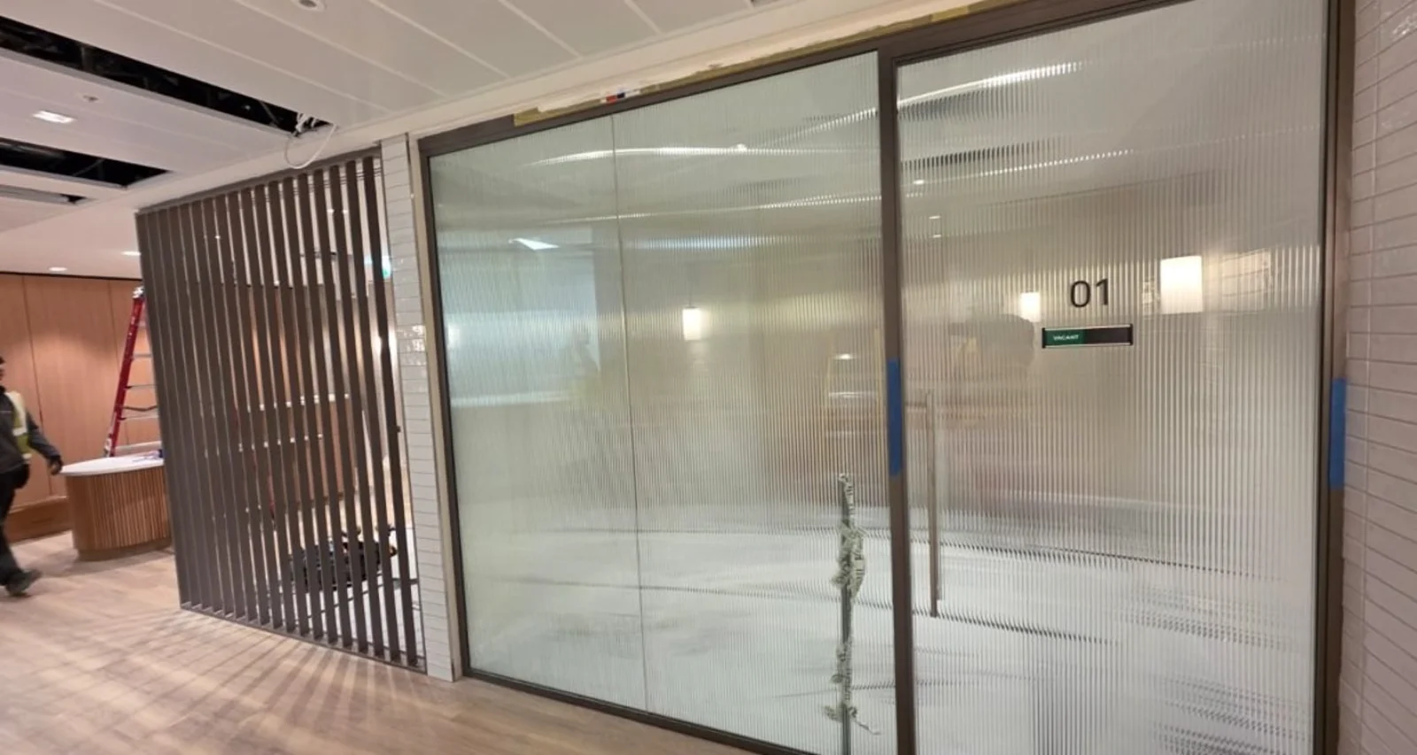 Bronze-framed partitioning with reeded glass to office 01, beside a screen of bronze fins.