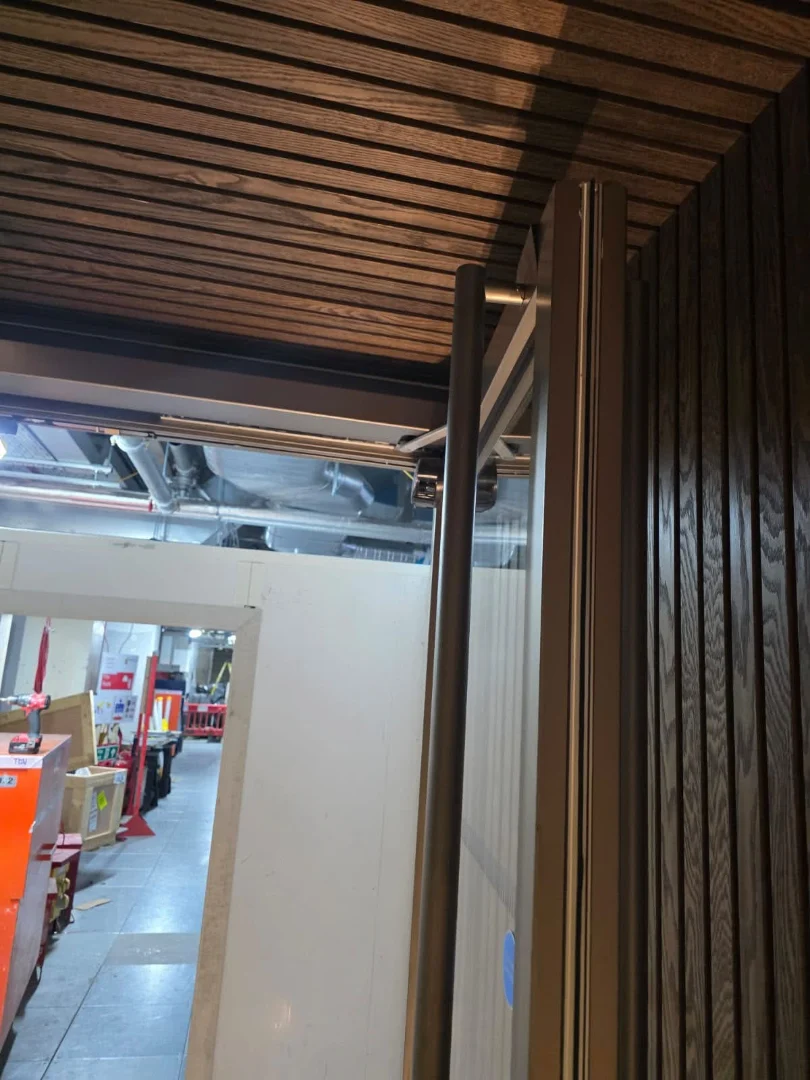 The head of a power-operated door, with its operator arm, under the timber-slatted ceiling.