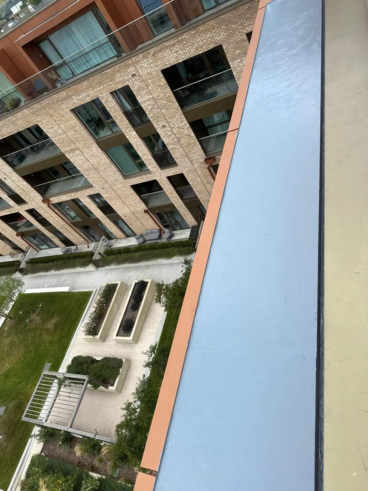 An elevated view of the completed parapet membrane and cladding trim, overlooking the landscaped courtyard below.